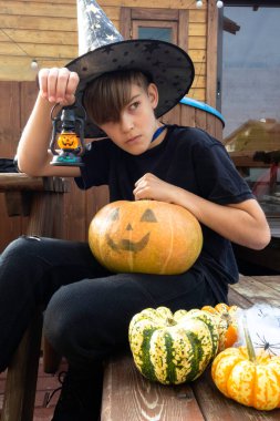 Cadılar Bayramı kostümlü çocuk, şapka ve sonbahar balkabakları ahşap terasta, cadılar bayramı, bayram ve çocukluk konsepti