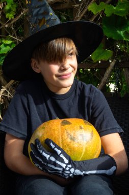 Cadılar Bayramı kostümlü çocuk, şapka ve sonbahar balkabakları ahşap terasta, cadılar bayramı, bayram ve çocukluk konsepti