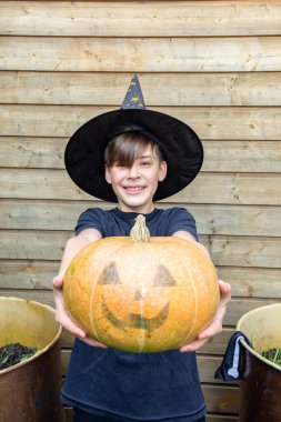 Ahşap arka planda Cadılar Bayramı balkabakları olan mutlu genç çocuk, bayram ve çocukluk konsepti