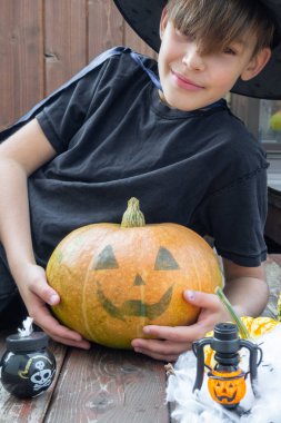 Cadılar Bayramı kostümlü çocuk, şapka ve sonbahar balkabakları ahşap terasta, cadılar bayramı, bayram ve çocukluk konsepti