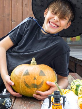Cadılar Bayramı kostümlü çocuk, şapka ve sonbahar balkabakları ahşap terasta, cadılar bayramı, bayram ve çocukluk konsepti