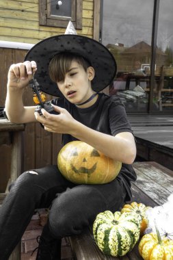 Cadılar Bayramı kostümlü, şapkalı ve sonbahar balkabaklı bir çocuk, ve ahşap terasta elinde lamba, cadılar bayramı, bayram ve çocukluk kavramı