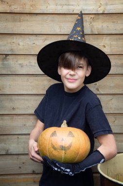 Cadılar Bayramı kostümlü çocuk, şapka ve sonbahar balkabakları ahşap terasta, cadılar bayramı, bayram ve çocukluk konsepti