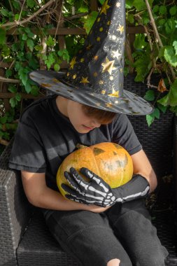 Cadılar Bayramı kostümlü çocuk, şapka ve sonbahar balkabakları açık terasta, cadılar bayramı, tatil ve çocukluk konsepti