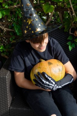 Cadılar Bayramı kostümlü çocuk, şapka ve sonbahar balkabakları açık terasta, cadılar bayramı, tatil ve çocukluk konsepti