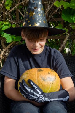 Cadılar Bayramı kostümlü çocuk, şapka ve sonbahar balkabakları açık terasta, cadılar bayramı, tatil ve çocukluk konsepti