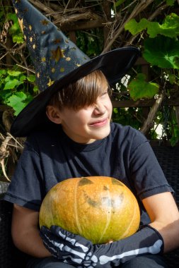 Cadılar Bayramı kostümlü çocuk, şapka ve sonbahar balkabakları açık terasta, cadılar bayramı, tatil ve çocukluk konsepti