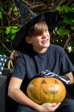 Cadılar Bayramı kostümlü çocuk, şapka ve sonbahar balkabakları açık terasta, cadılar bayramı, tatil ve çocukluk konsepti