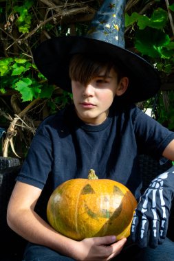 Cadılar Bayramı kostümlü çocuk, şapka ve sonbahar balkabakları açık terasta, cadılar bayramı, tatil ve çocukluk konsepti