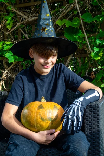 Cadılar Bayramı kostümlü çocuk, şapka ve sonbahar balkabakları açık terasta, cadılar bayramı, tatil ve çocukluk konsepti