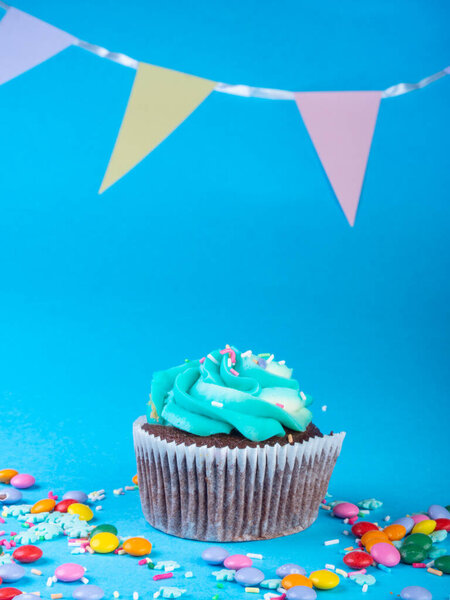 Cupcake with whipped cream in a blue background, decorated with sugar snowflakes, sprinkles, colorful candies