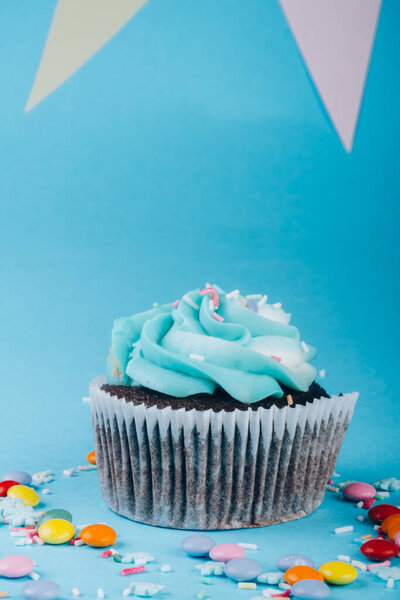 Cupcake with whipped cream in a blue background, decorated with sugar snowflakes, sprinkles, colorful candies