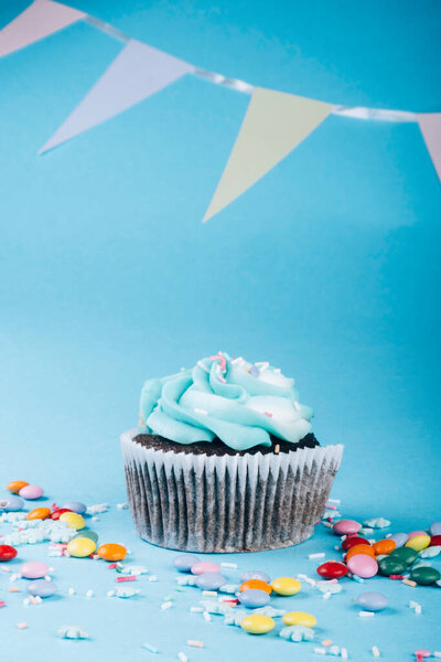 Cupcake with whipped cream in a blue background, decorated with sugar snowflakes, sprinkles, colorful candies