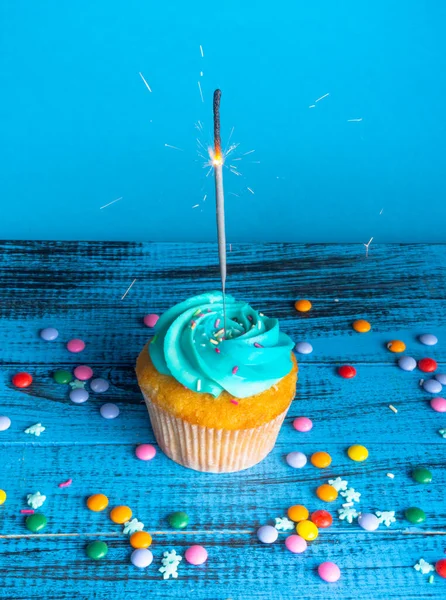 Birthday or christmas cupcake with a sparkler, against a blue background, dark toned, selective focus