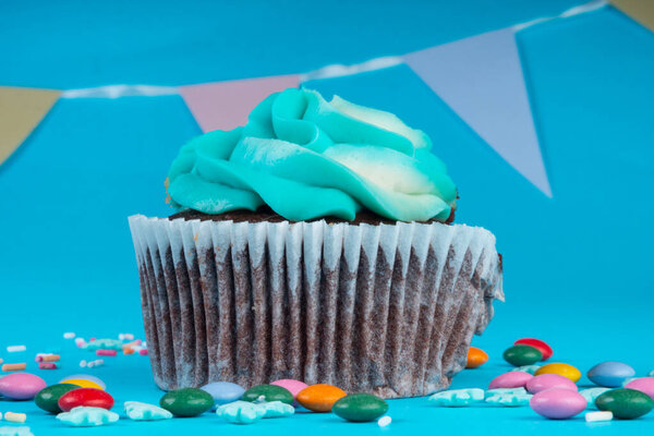 Chocolate Cupcake with whipped cream in a blue background, decorated with sugar snowflakes, sprinkles, colorful candies, holiday concept, greeting card