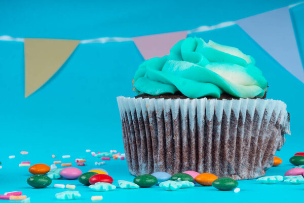 Chocolate Cupcake with whipped cream in a blue background, decorated with sugar snowflakes, sprinkles, colorful candies, holiday concept, greeting card