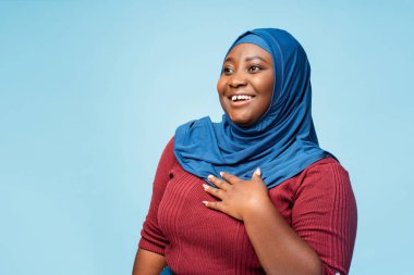 Otantik, çekici, geleneksel tesettürlü Müslüman kadın mavi arka planda izole edilmiş. Gülümseyen iş kadını başka tarafa bakıyor, reklam konsepti
