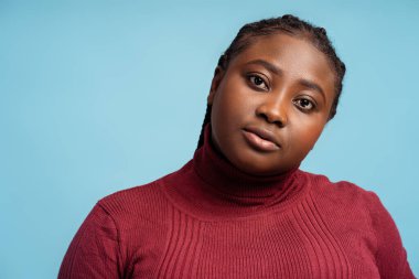 Ciddi Afro-Amerikan kadın şık kırmızı süveter giyiyor kameraya bakıyor, mavi arka planda izole poz veriyor, fotokopi odası. Reklam konsepti, moda