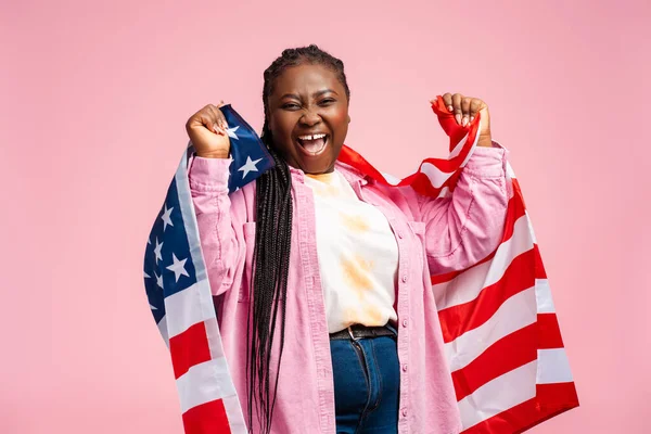 Attractive African American woman holding American flag rejoicing at election results, looking at camera. Emotional plus size female supporter. American election day concept