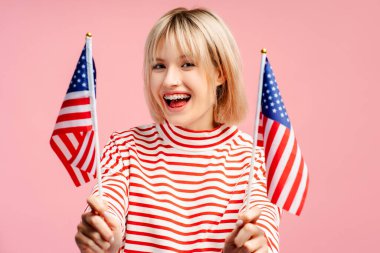 Gülümseyen, sarı saçlı, elinde Amerikan bayrağı olan genç ve güzel bir kadın kameraya bakıyor. Mavi arka planda tek başına duran kadın destekçi. Amerikan bağımsızlık günü konsepti