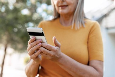 Yaşlı bir kadın cep telefonu kullanırken dışarıda eğleniyor, bağlı kalıyor ve modern teknolojiyi kolayca kucaklıyor.