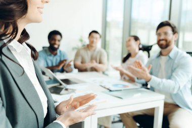 Çok ırklı iş adamları modern ofis toplantı odasında başarılı bir sunum yaptıktan sonra iş kadınını alkışlayarak başarı ve takım çalışmasını kutluyorlar.