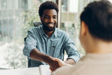 Ofisteki bir toplantıda gülümseyen Afrikalı Amerikalı işadamı ortağıyla tokalaşıyor, başarılı bir anlaşma yapıyor ya da yeni bir işbirliği başlatıyor. Buluşma konsepti