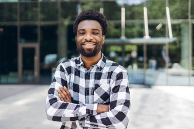 Modern bir ofis binasının önünde kollarını kavuşturarak duran neşeli bir Afro-Amerikan iş adamının portresi profesyonel kariyerinde kendine güveni ve başarısı var. İş konsepti