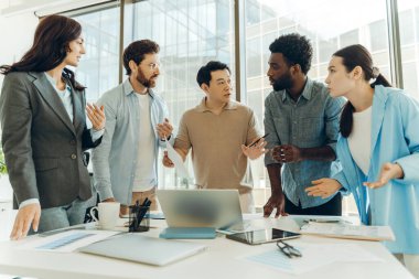 Beş iş adamından oluşan çeşitli bir grup modern ofis ortamında proje üzerinde işbirliği yaparak çizelgeler ve dizüstü bilgisayarlarla bir masanın etrafında tartışıyorlar. İş konsepti