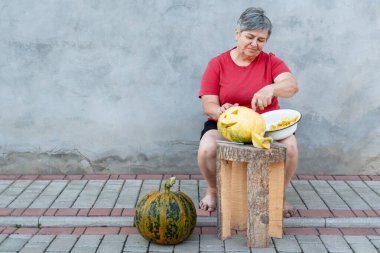 Kıdemli kadın Cadılar Bayramı kutlaması için balkabağından fener yapıyor tahta taburede oturuyor.