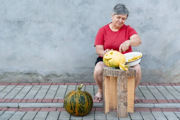 Kıdemli kadın Cadılar Bayramı kutlaması için balkabağından fener yapıyor tahta taburede oturuyor.