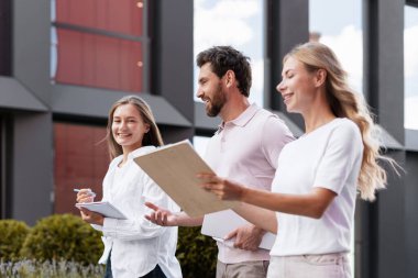İş adamları bir ofis binasının dışında yürüyor, belgeleri tutarken projeleri tartışıyor, işbirliği ve takım çalışması sergiliyor