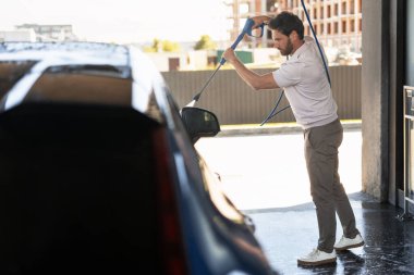 Otomobil yıkamada yüksek basınçlı su jeti kullanan bir adam, parlak bir son için aracını sabun ve köpükle iyice temizliyor.
