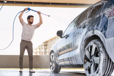 Adam arabasını temizlemek için yüksek basınçlı su jeti kullanıyor, araçtaki toz ve kiri temizlerken köpüklü sprey yaratıyor.