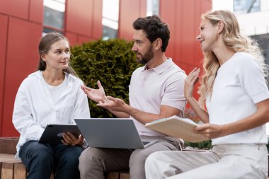 Meslektaşlar, proje stratejilerini tartışırken, takım çalışmalarını ve işbirliğini teşvik etmek için açık hava toplantılarına katılıyor, dizüstü bilgisayarlardan ve tabletlerden faydalanıyor