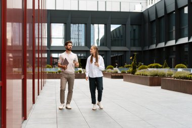 Ofis dışında bir proje hakkında konuşurken kahve içen iki meslektaş, modern bir şehir ortamında işbirliğini teşvik ediyor.