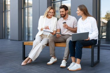 İş ekibi dışarıda birlikte çalışıyor, verileri analiz ediyor ve stratejiyi tartışıyor, dizüstü bilgisayarları, akıllı telefonları kullanıyor ve notlar alıyor.