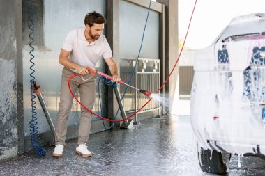 Yüksek basınçlı su jeti kullanan bir adam otomobil yıkama istasyonunda arabasındaki sabunu durulamak için kullanıyor.