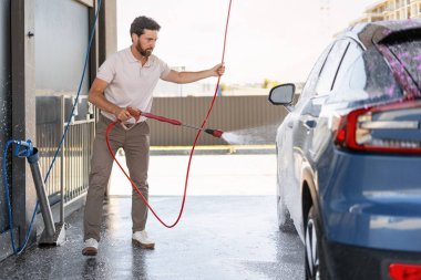 Araba yıkama işçisi yüksek basınçlı su ve sabunu kullanarak aracın iyice temizlenmesini sağlıyor.