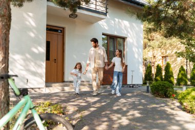 Baba ve iki kız el ele tutuşarak evden ayrılıyorlar, evlerinin önünde yürüyorlar, aile gezisine hazırlanıyorlar, bir bisiklet ve scooterla yakınlarına park etmişler. Ebeveynlik kavramı