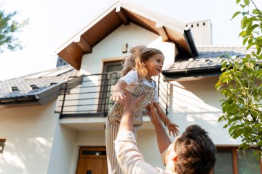 Mutlu bir baba kızını havaya kaldırıyor, yeni bir ev almayı kutluyor, bahçelerinde güneşli bir günün tadını çıkarıyor, aileyi, mutluluğu ve Amerikan rüyasını simgeliyor.