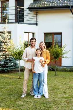 Gülümseyen ebeveynler ve kızları, yemyeşil ve aile birliğinin sıcaklığıyla çevrili yeni modern evlerinin bahçesinde güneşli bir günün tadını çıkarıyorlar. Ebeveynlik kavramı