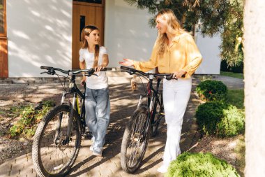 Gülümseyen anne ve kız bisikletleriyle evlerinin bahçesinde yürüyor, sohbet ediyorlardı.