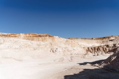 Kireç taşı ocağının panoramik görüntüsü, temiz mavi gökyüzünün altında çıkarılmış materyal yığınlarıyla çıkarma çalışmalarını gösteriyor.