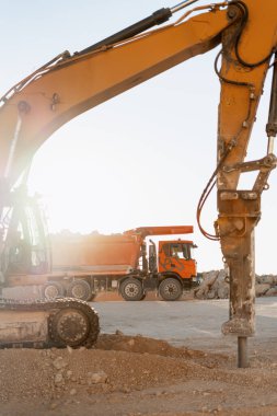 Kazıcı gün batımında asfaltı kırıyor. Yol inşaatı sırasında atık madde taşıyan bir kamyonla.