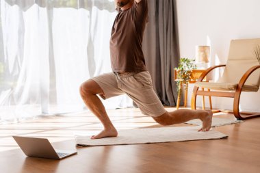 Bilgisayarda online dersi takip eden, sanal fitness yoluyla sağlık ve sağlığı destekleyen bir adam evde yoga yapıyor.
