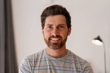 Ofisinde durmuş, gülümseyen, kendine güvenen bir iş adamının portresi, pozitif bir ifadeyle kameraya bakıyor.