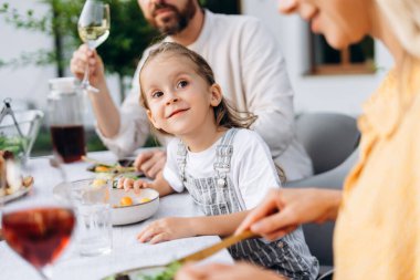 Neşeli bir bahçede ailesiyle öğle yemeğinin keyfini çıkarırken, sıcak yaz güneşinin altında birlikte geçirdiğimiz güzel anları ve kahkahaları seyreden mutlu küçük kız. Şükran Günü konsepti