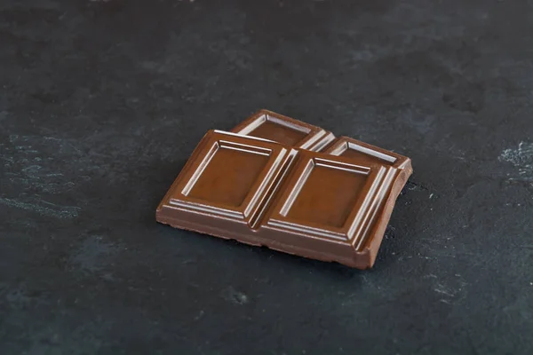 Slices of dark chocolate over black background with copy space