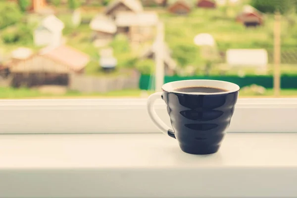 One cup of coffee for breakfast over white window sill with beautiful nature view, toned photo with copy space